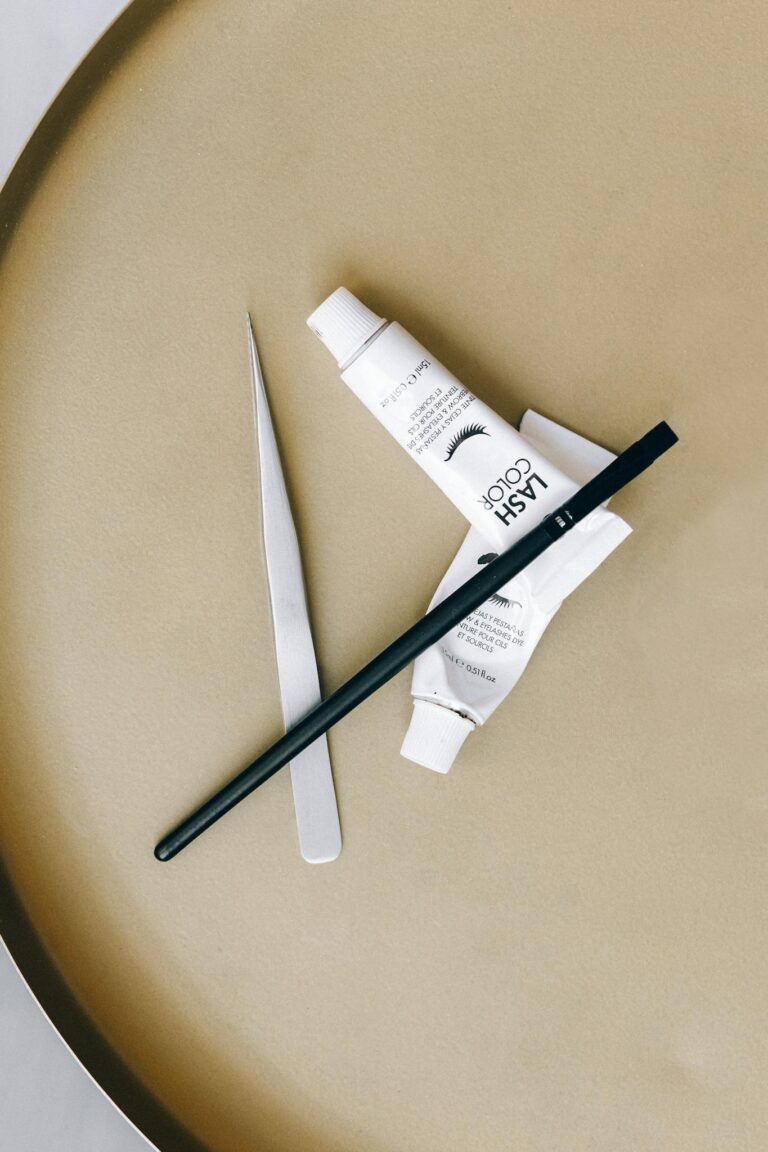 Stylish flat lay of eyelash tint and tools on a beige surface, ideal for beauty concepts.